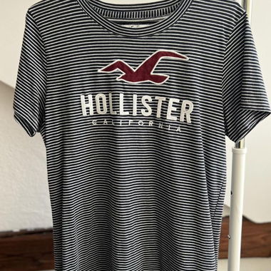T-shirt manica corta Hollister California a righe blu navy e bianco con grande uccello rosso e applicazione logo bianca sul petto. Taglia M. Realizzato in 60% cotone e 40% poliestere, tessuto jersey morbido. In buone condizioni, usato, senza difetti visibili.