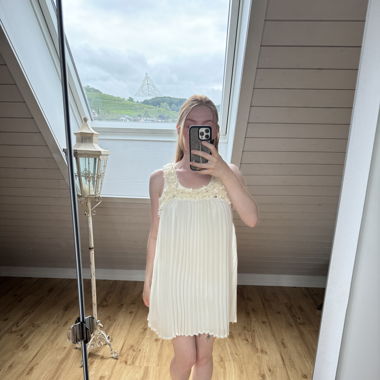 Cremiges Kleid mit Plisseefalten und Blumenbesatz